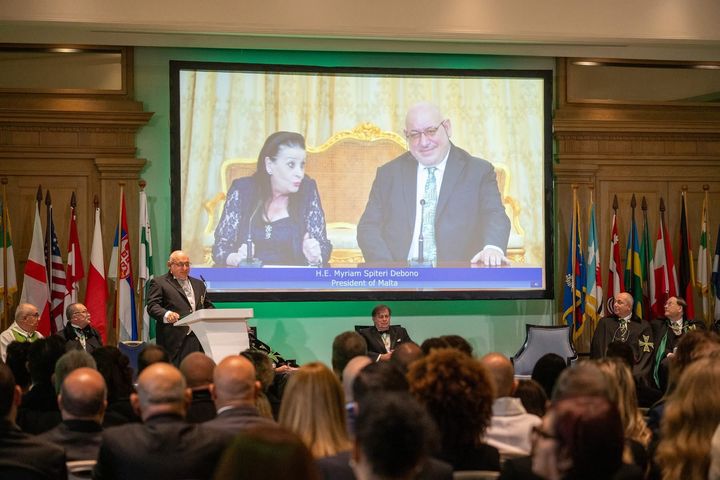 The Grand Chancellor, H.E. Massimo J. Ellul, at the lectern, with the President of Malta on the screen.